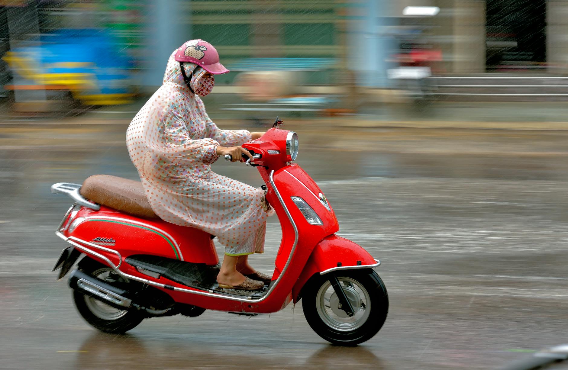 Kobieta na czerwonym skuterze w deszczu na miejskiej ulicy