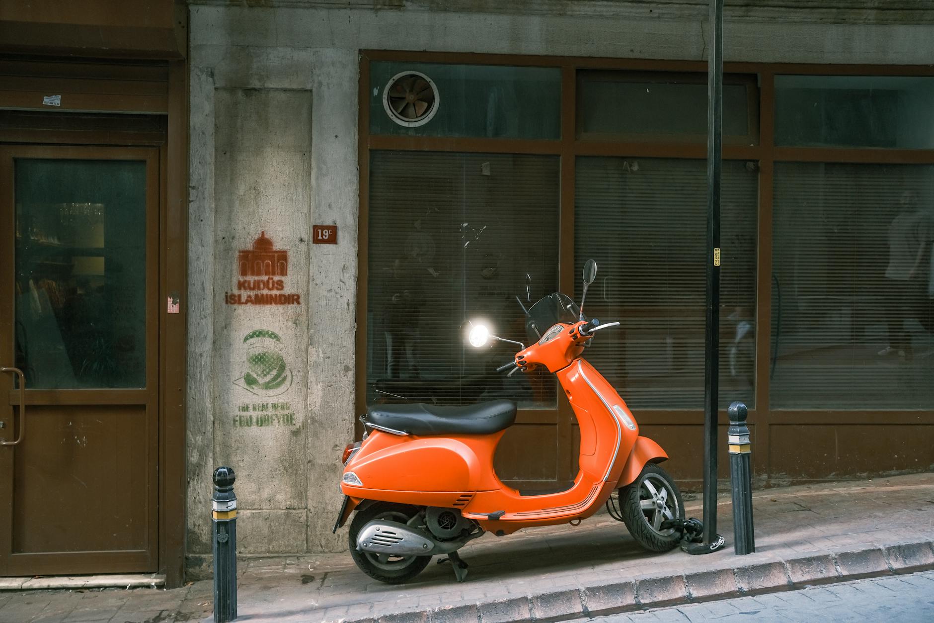 Pomarańczowy skuter Peugeot zaparkowany przy cichej, miejskiej ulicy